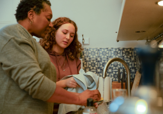 Close up shot of female adult washing the dishes in the kitchen, with a teenage girl who is drying dishes.