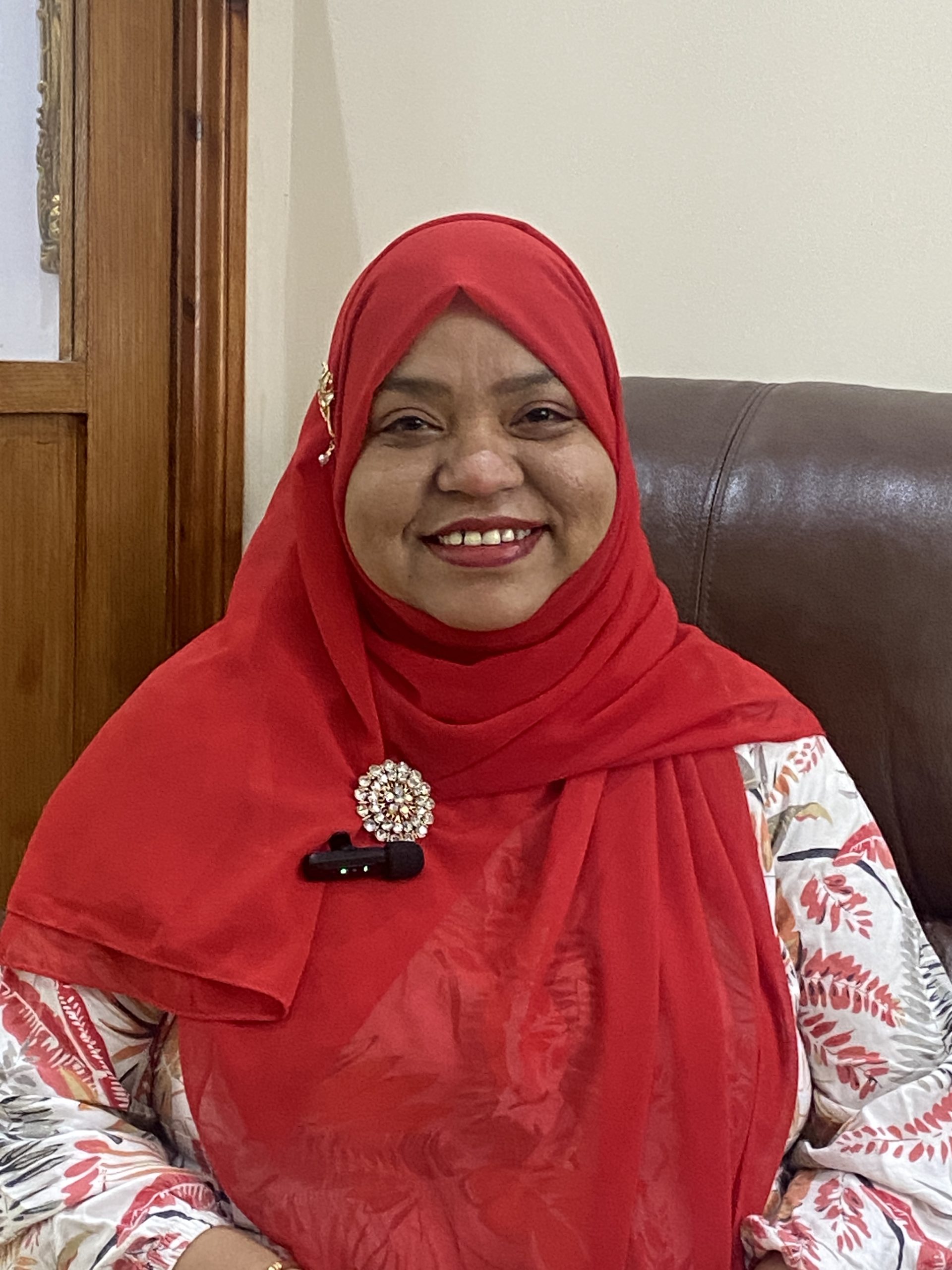Rohima smiling at the camera wearing a red headscarf and flowery shirt