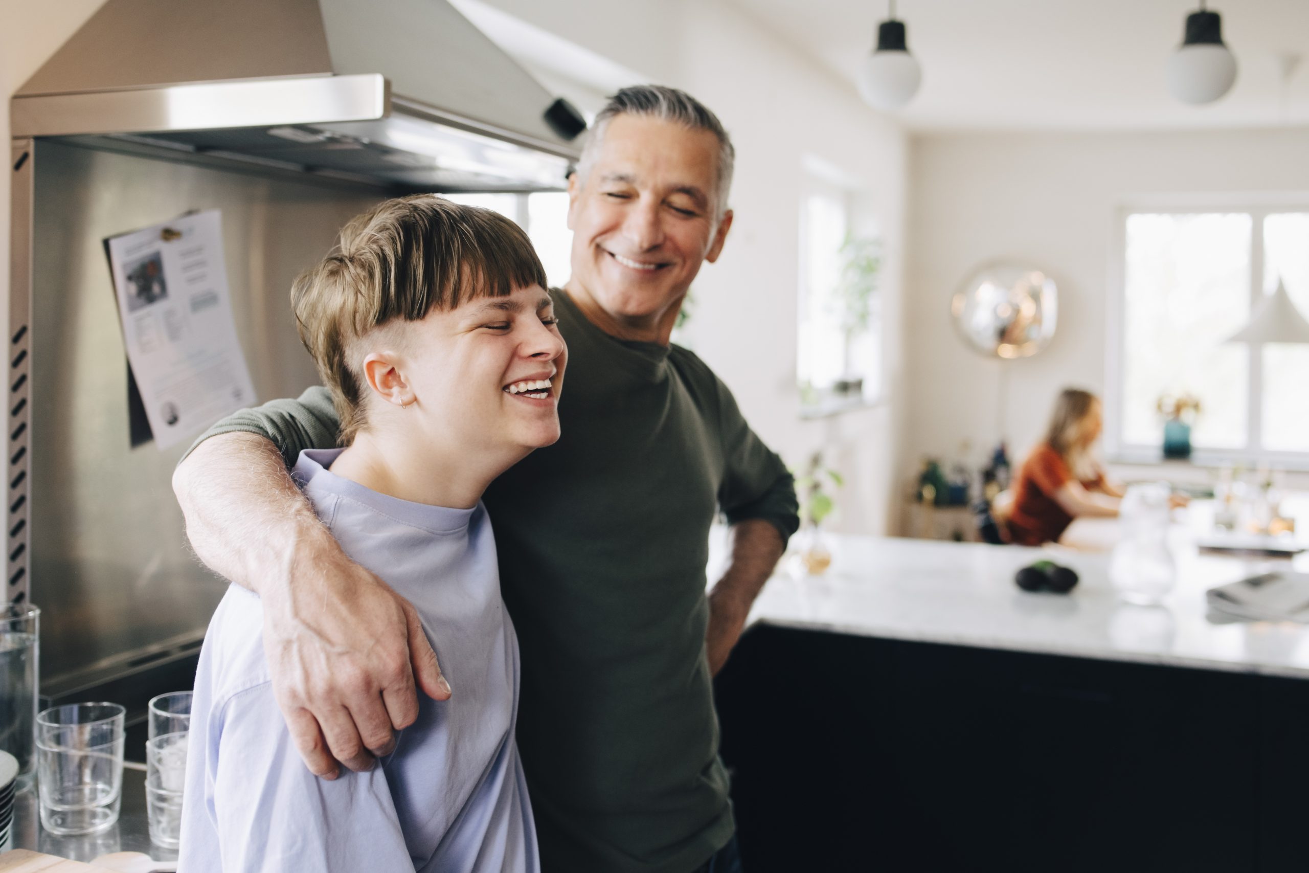 male foster carer with arm around happy fostered child in the kitchen