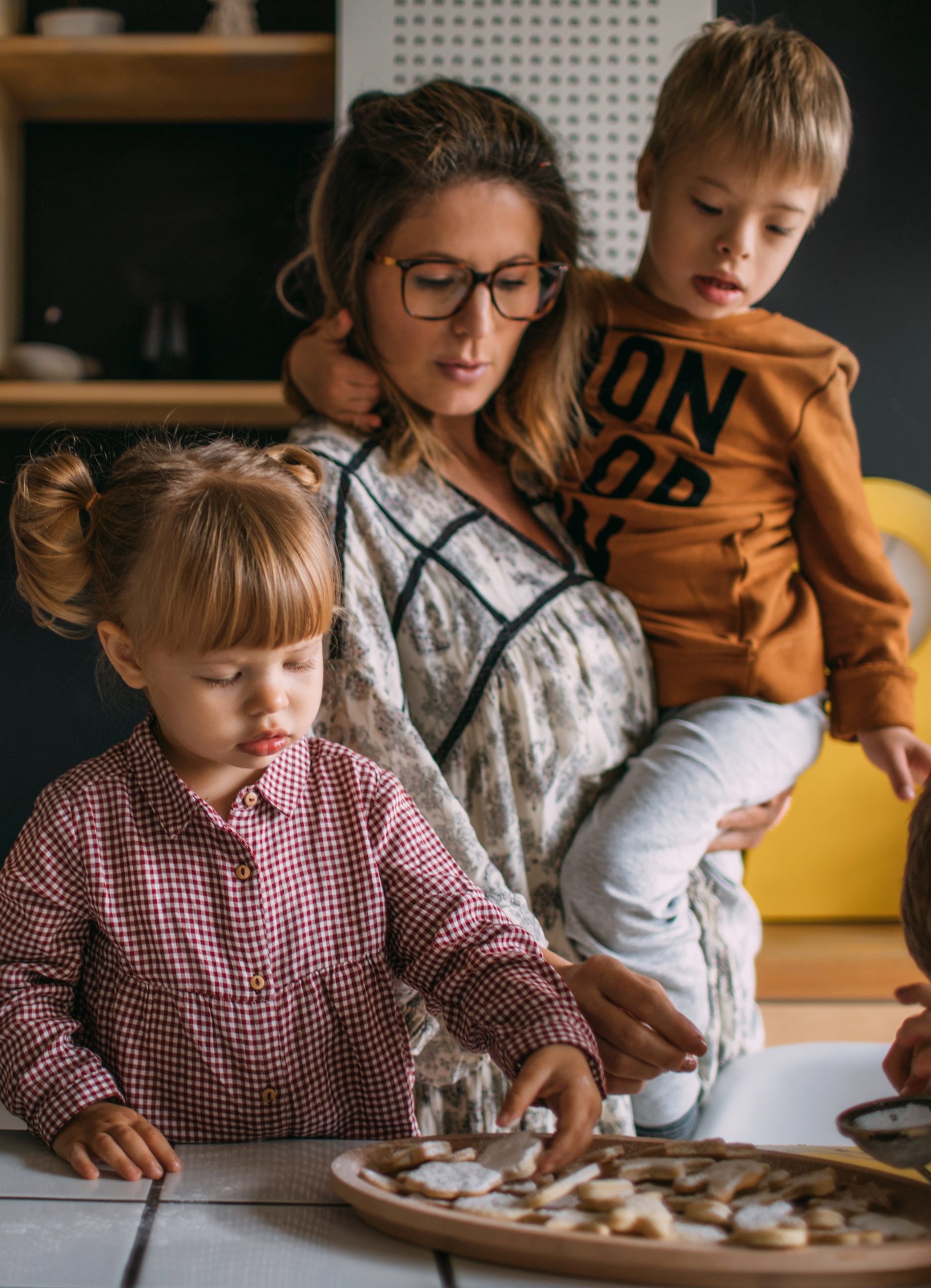 foster carer holding one foster child with another foster child in front of them trying out home made biscuits